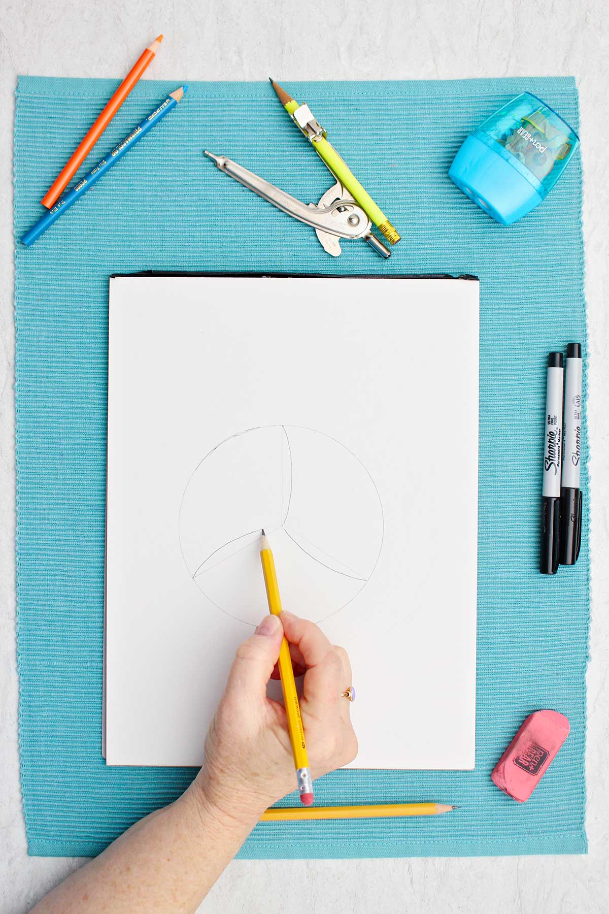 Pessoa esboçando linhas de detalhe no desenho do vôlei com um lápis.