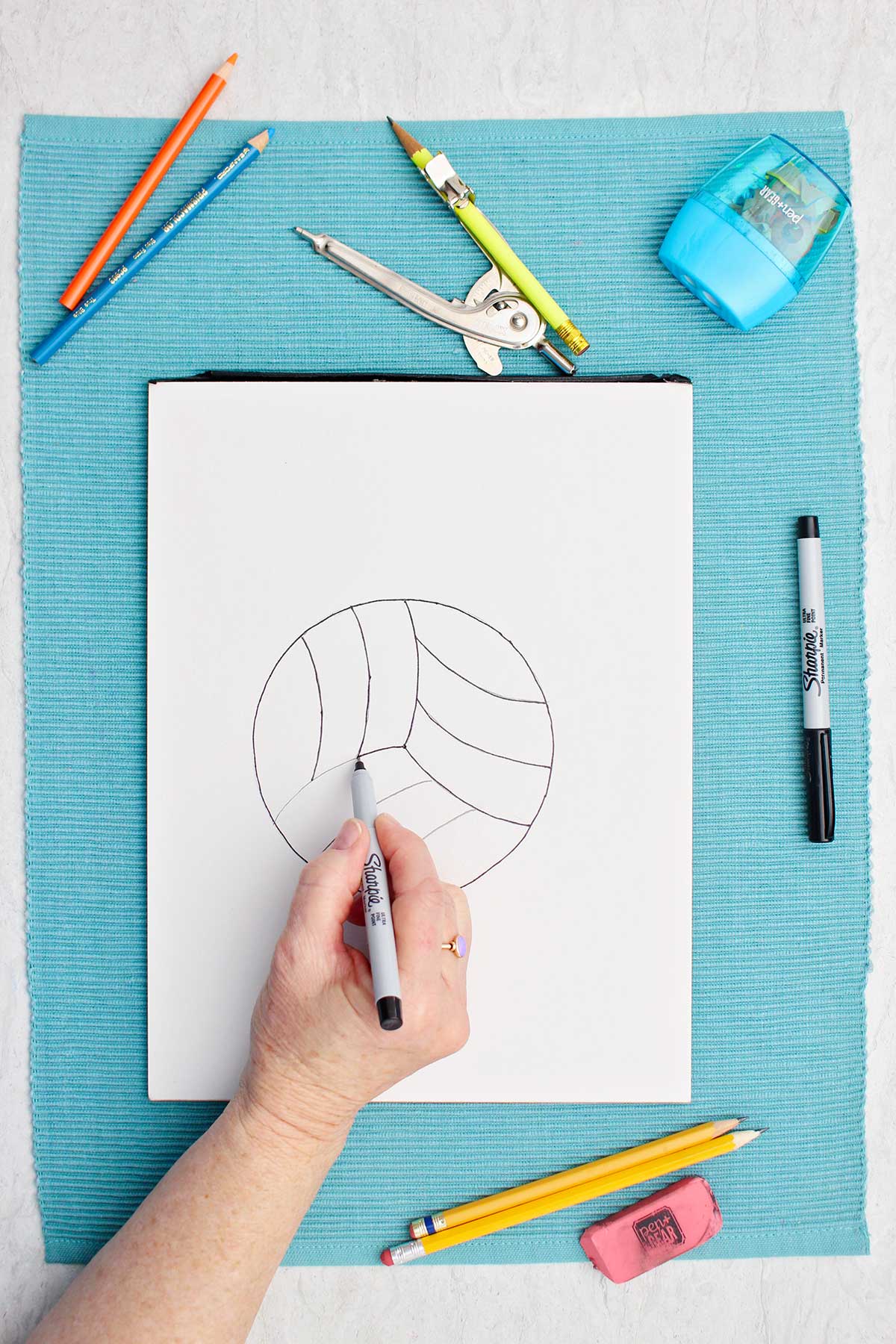 Uma pessoa traçando sobre linhas de lápis com um marcador no desenho de vôlei.