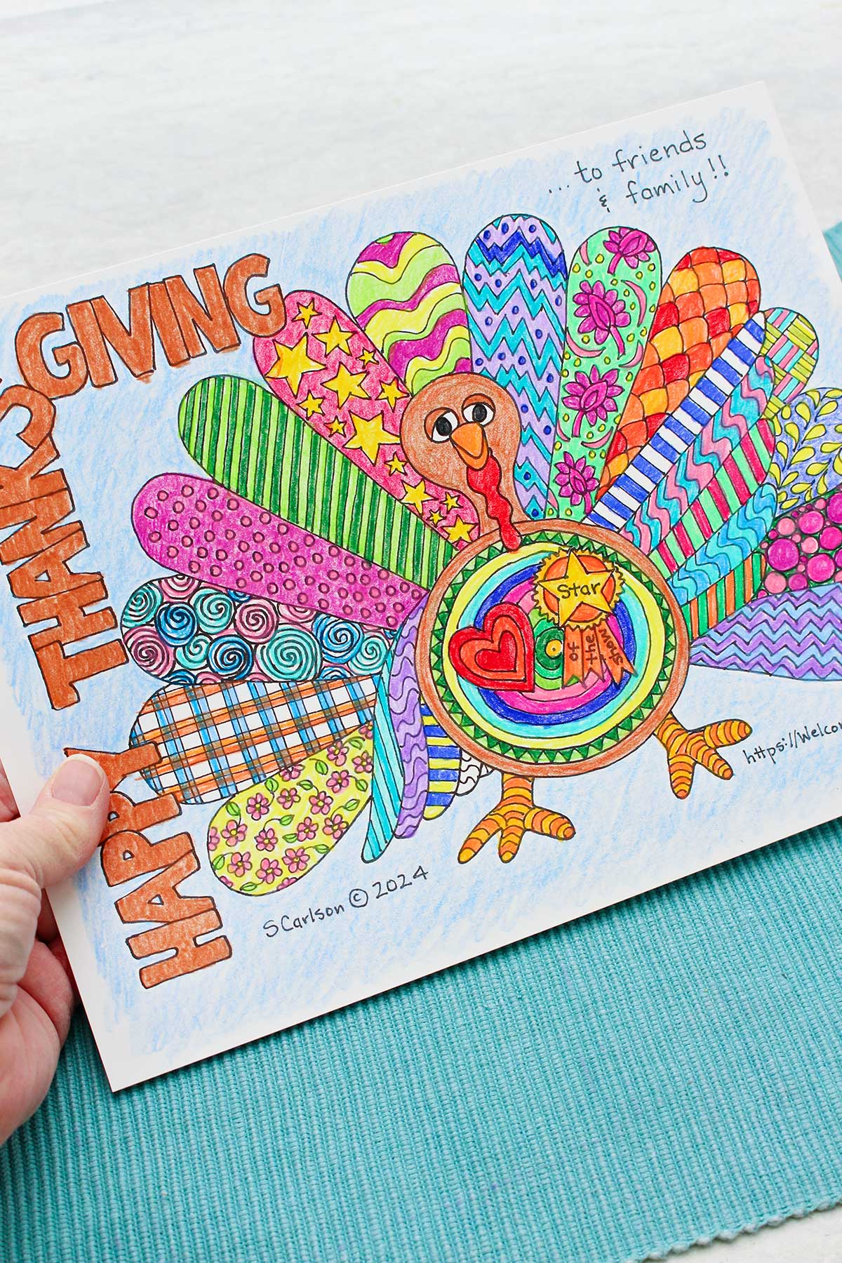Uma pessoa segurando uma página de colorir de Ação de Graças dizendo 'Feliz Ação de Graças' e um peru com asas coloridas e padronizadas.