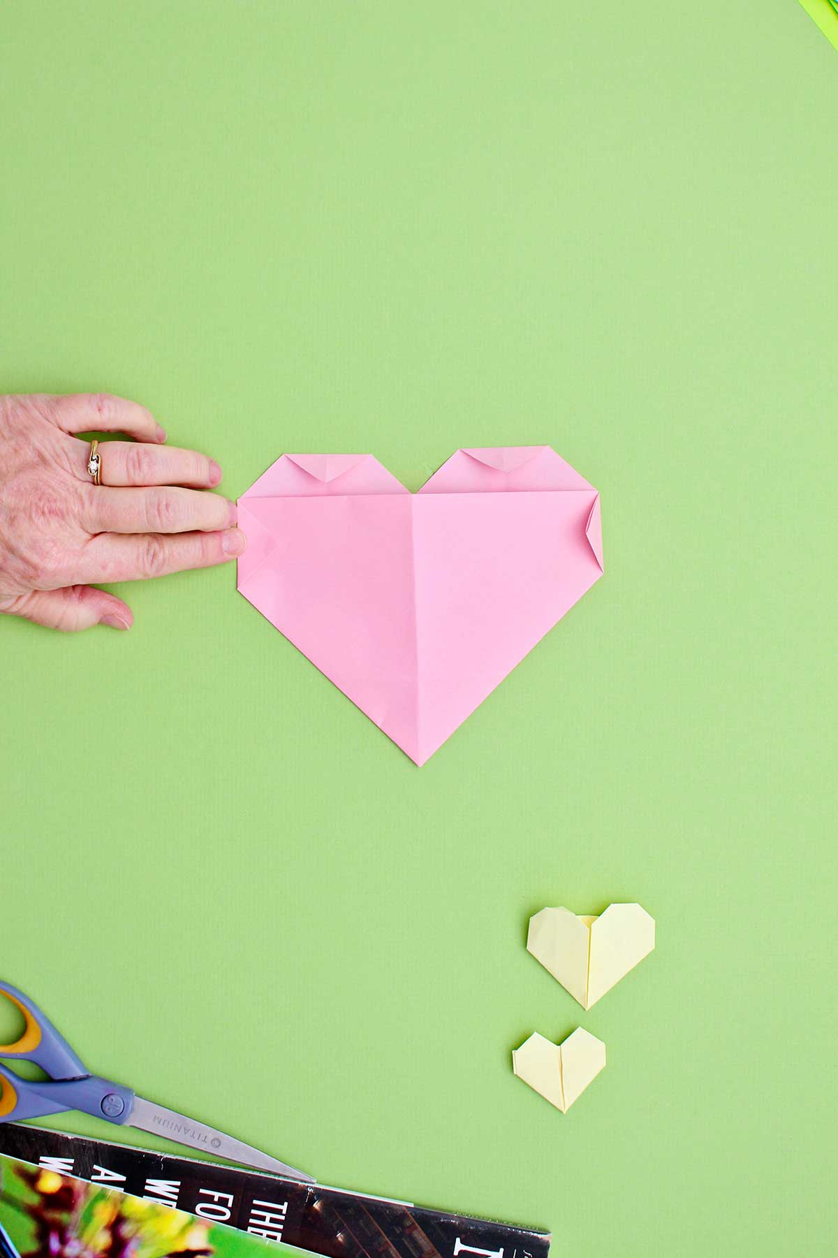Uma pessoa dobrando os triângulos laterais para completar seu coração de origami.