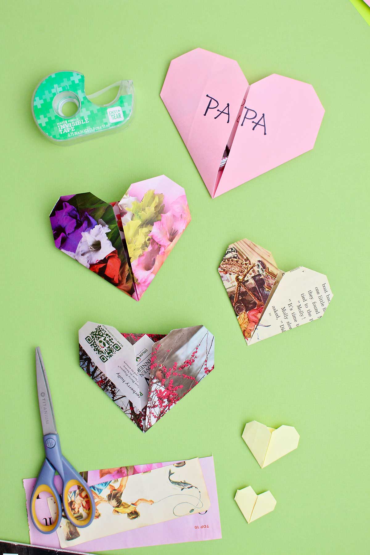 Quatro corações de origami em um fundo verde com tesouras e fita por perto.