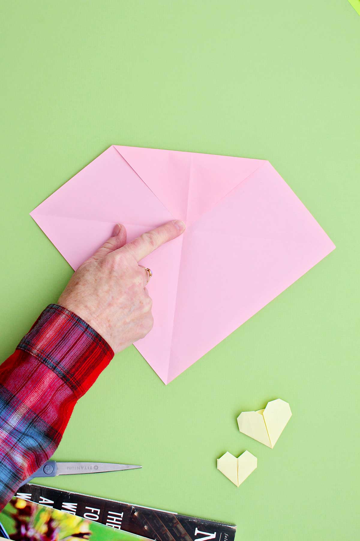Dobrando o canto superior de um pedaço de papel rosa para baixo, em direção ao centro, para criar a parte superior de um coração.