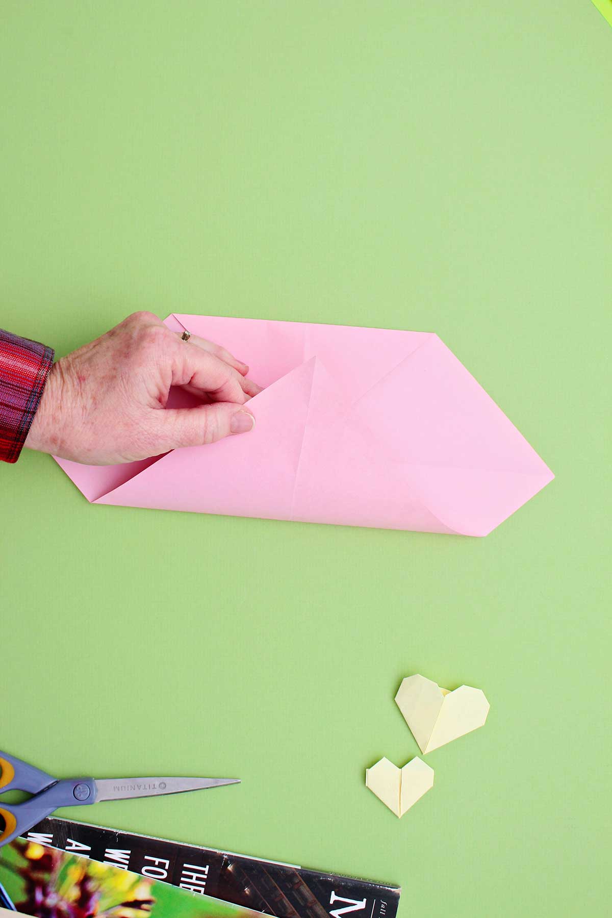 Pessoa dobrando o canto de um pedaço de papel rosa para cima, para encontrar a parte superior dobrada.