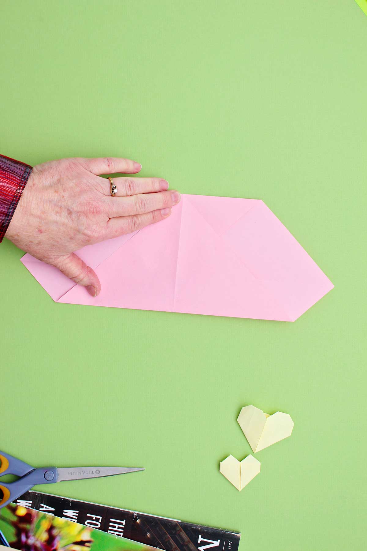 Pessoa dobrando o canto de um pedaço de papel rosa para cima, para encontrar a parte superior dobrada.