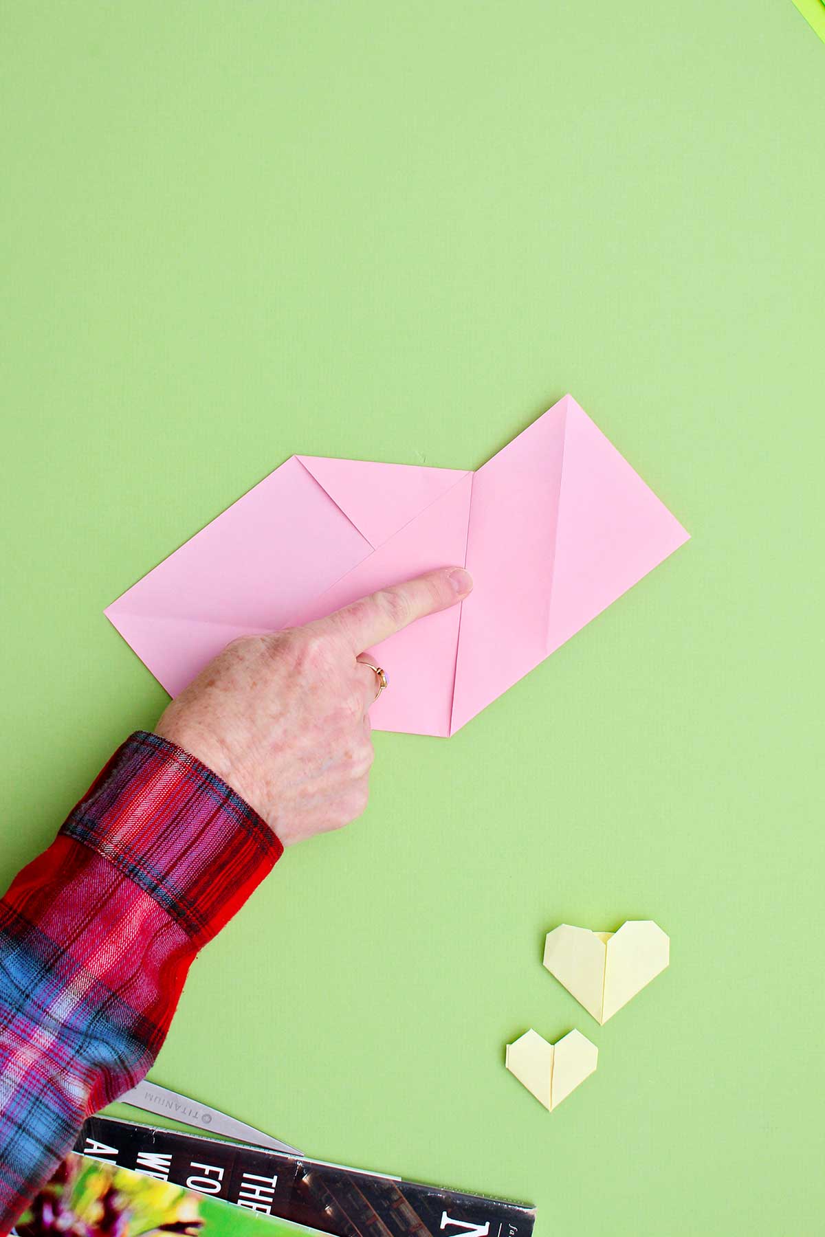 Pessoa mostrando um coração de origami rosa com um vinco central.