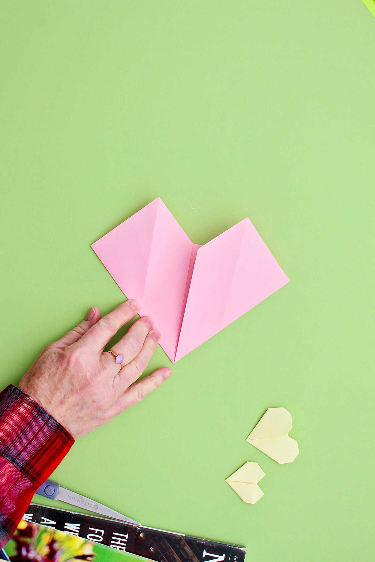 Uma pessoa dobrando as laterais para criar o corpo do coração de origami.