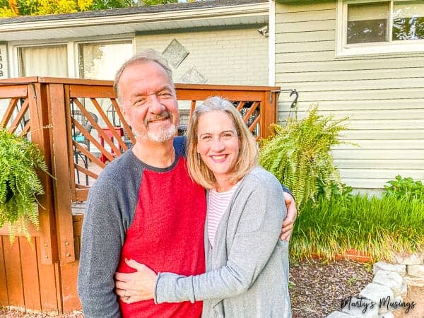 marido e mulher sorrindo enquanto se abraçam na frente da casa