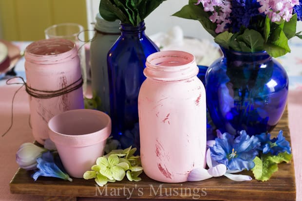 Uma xícara de café e um vaso de flores sobre uma mesa, com um pote mason jar