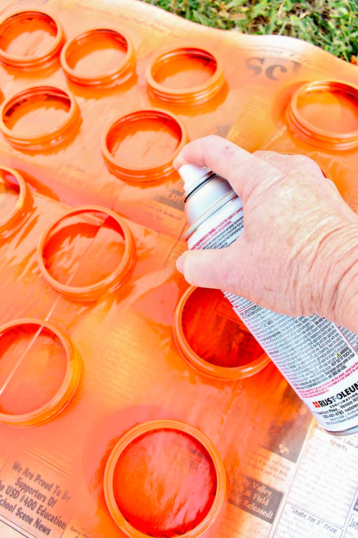 Pessoa pintando tampa de pote de conserva de laranja do lado de fora em um pedaço de papel jornal.