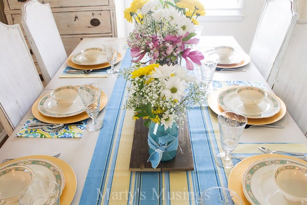 Uma mesa com um vaso de flores sobre um prato, com azul e primavera
