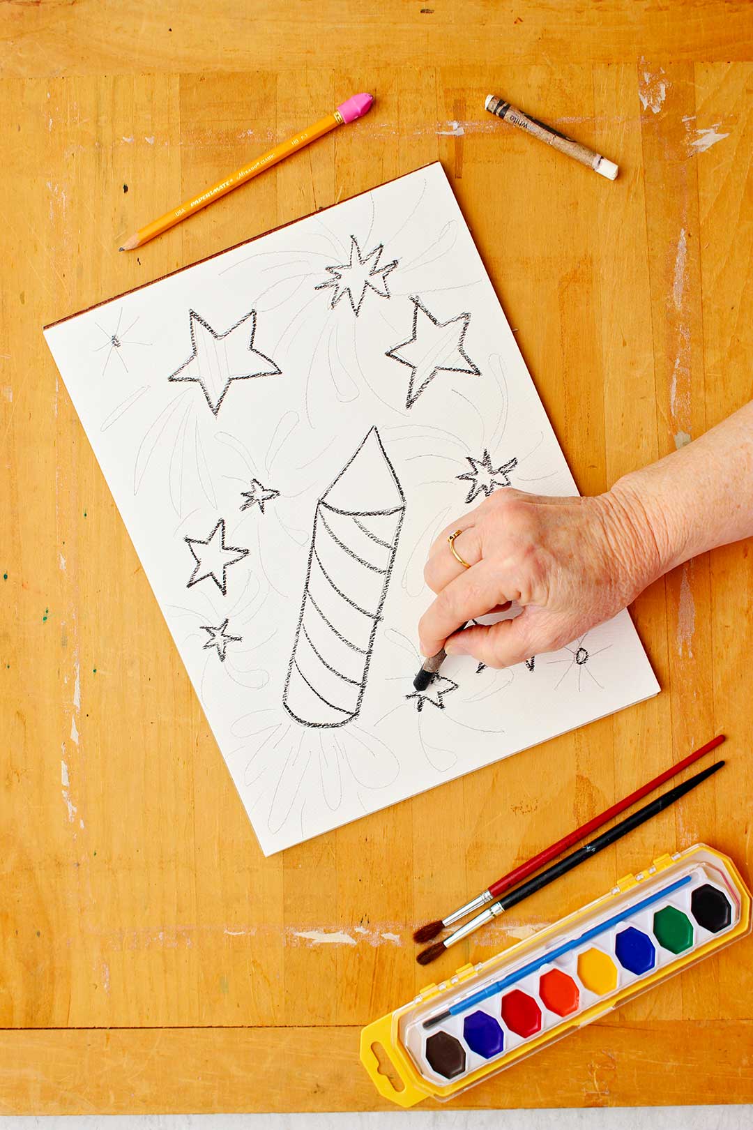Desenhando estrelas com giz de cera preto no papel.
