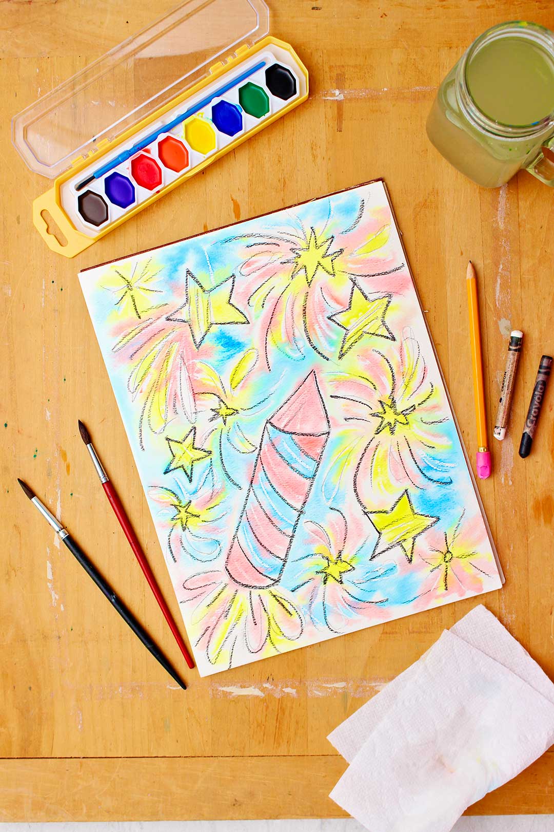 A resistência em aquarela completa repousa sobre uma mesa de madeira com aquarelas, um copo d'água, pincéis e toalhas de papel por perto.