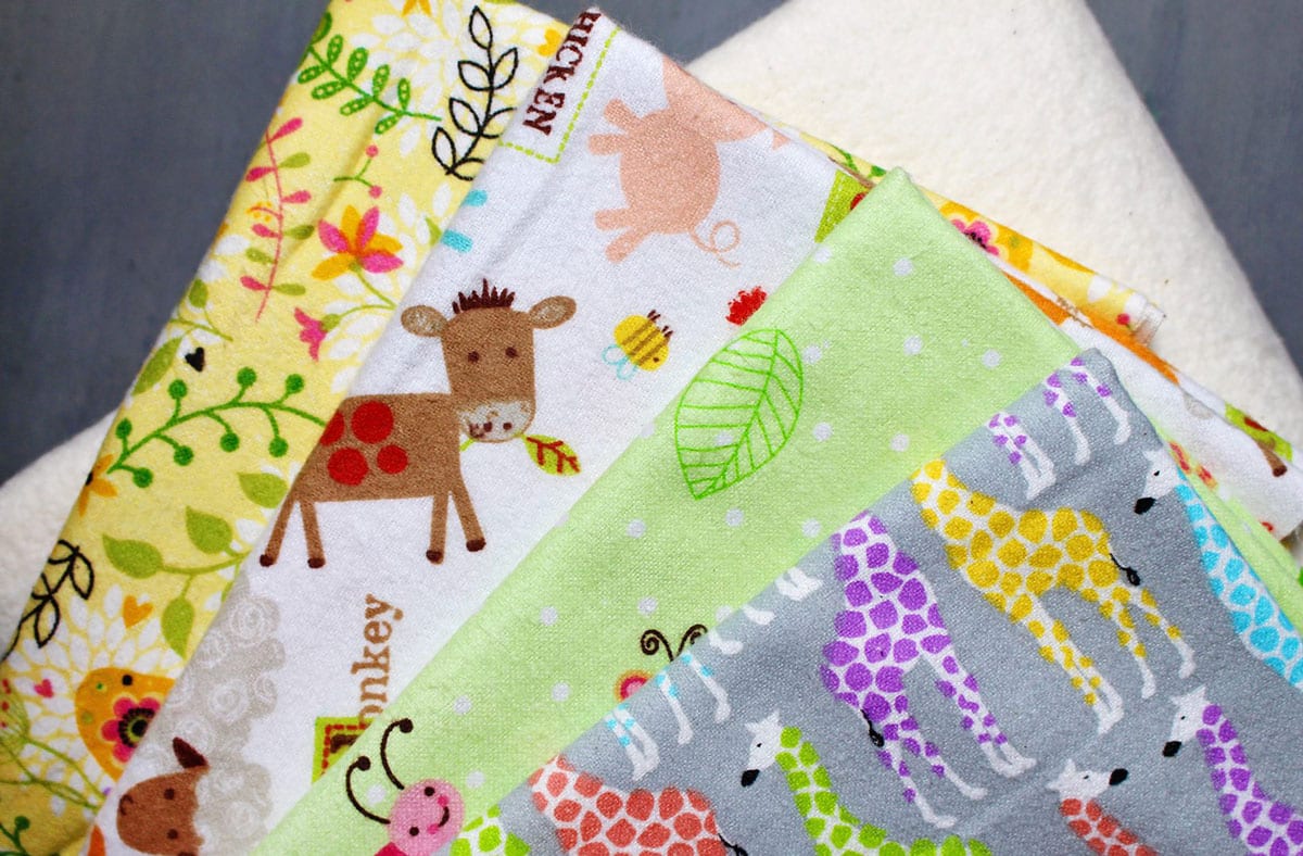 Uma pilha de estampas de tecido de feltro colorido prontas para serem costuradas em toalhas de boca de bebê.
