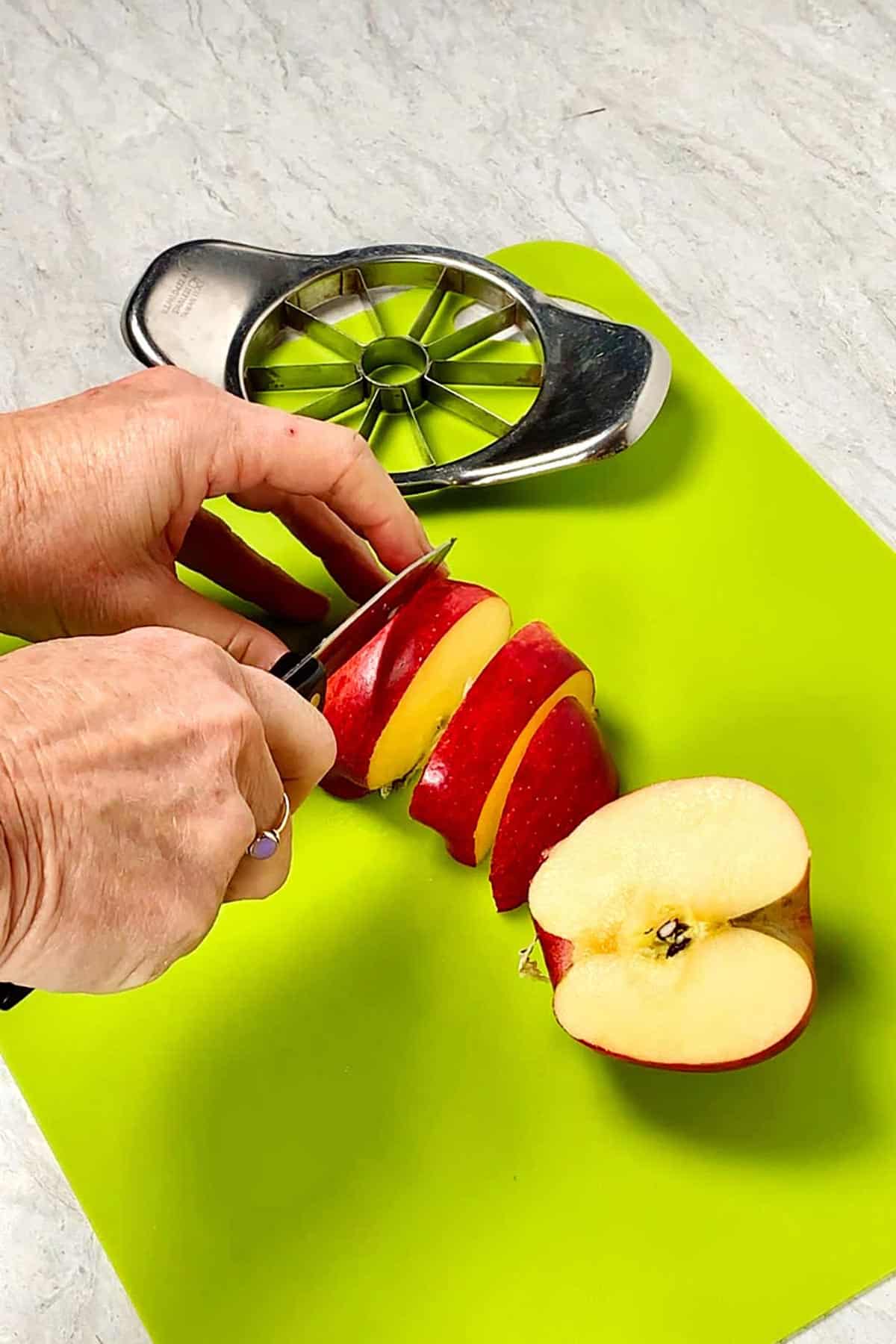 Pessoa fatiando maçãs com uma faca em uma tábua de corte verde brilhante.