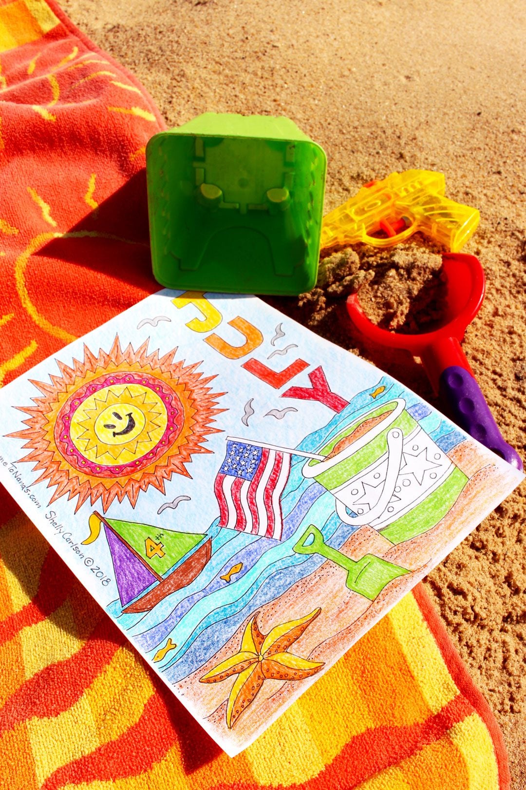 Página de colorir de julho finalizada em toalha de praia na areia com lápis de cor ao redor.