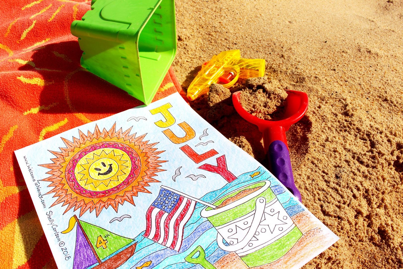 Página de colorir de julho finalizada em toalha de praia na areia com lápis de cor ao redor.