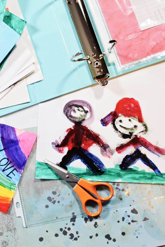 Pintura de uma criança de duas pessoas de mãos dadas, com tesouras, um fichário e papel de scrapbook nas proximidades.