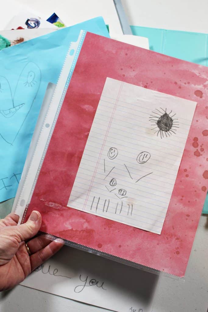 Desenho a lápis de uma criança de uma família e sol, montado em papel de scrapbook e dentro de um protetor de folha.