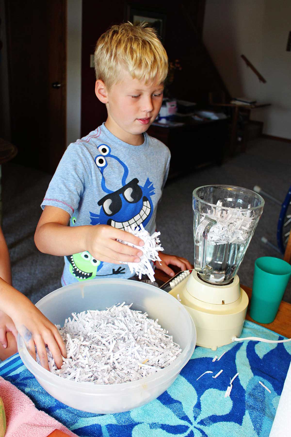Uma criança adicionando papel picado a um liquidificador com água.