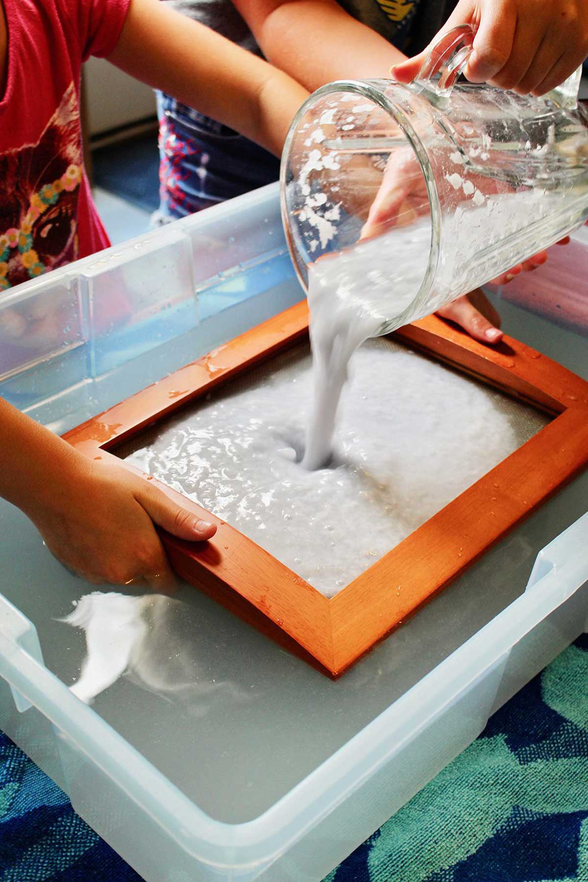 Despejando papel batido e água em um molde e moldura em uma caixa de água.