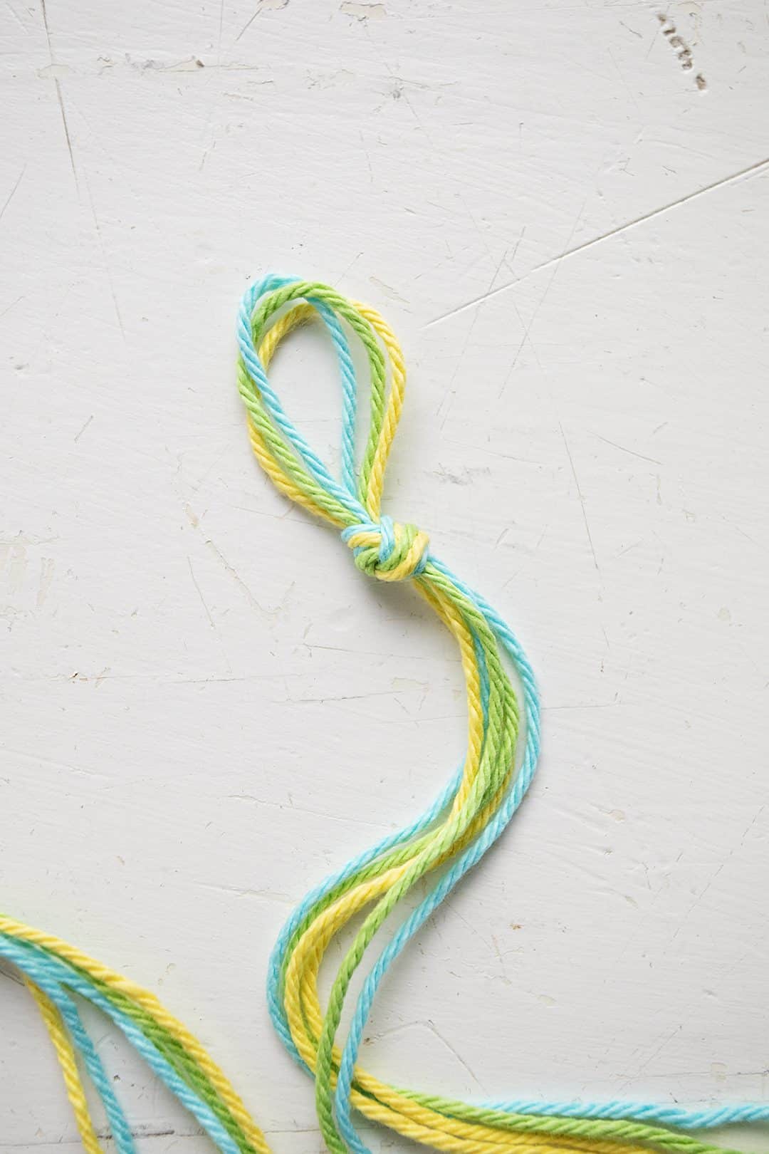 Uma pulseira em padrão Chevron sendo feita com cordão azul, verde e amarelo.