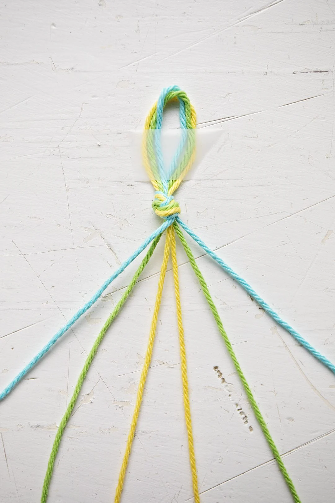 Uma pulseira com padrão Chevron sendo feita com fios azuis, verdes e amarelos.