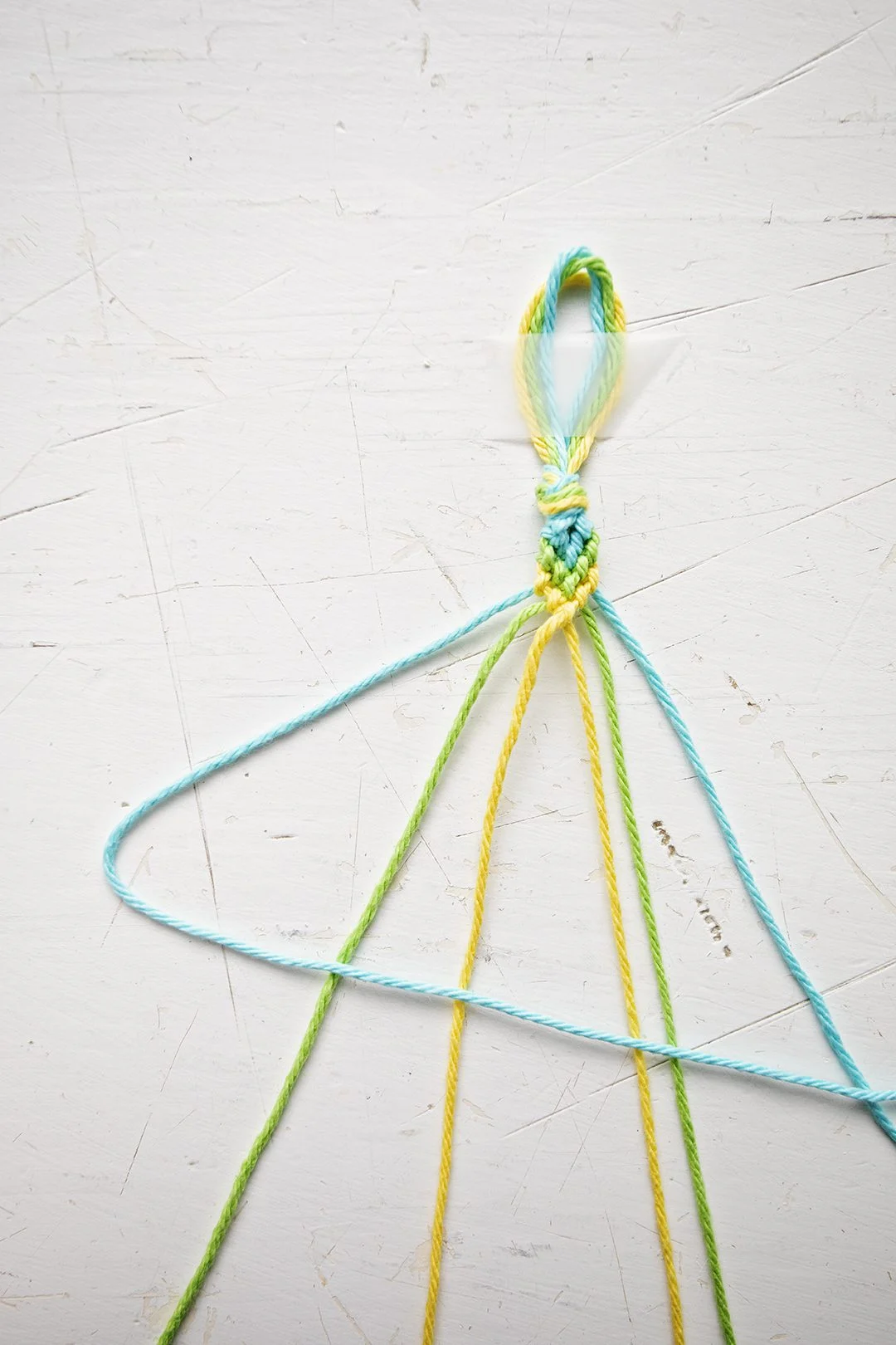 Uma pulseira com padrão Chevron sendo feita com fios azuis, verdes e amarelos.