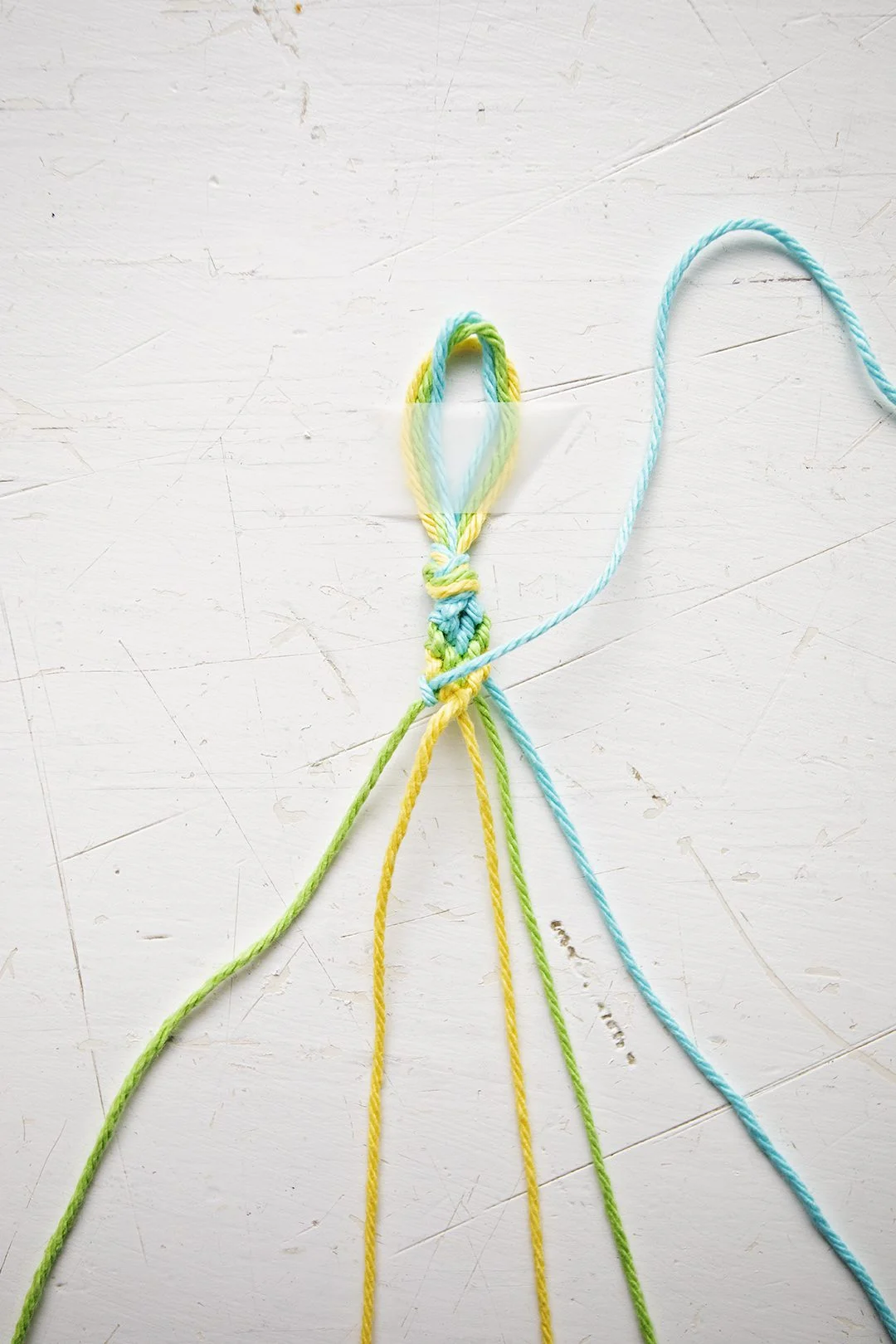 Um padrão de pulseira em Chevron sendo feito a partir de fios azuis, verdes e amarelos.