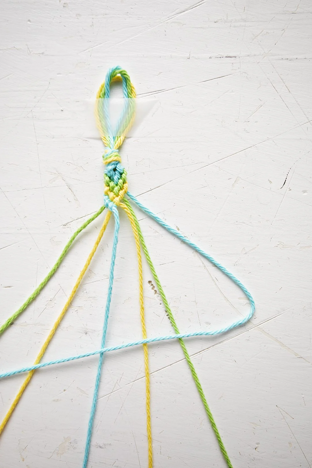 Um padrão de pulseira em Chevron sendo feito a partir de fios azuis, verdes e amarelos.