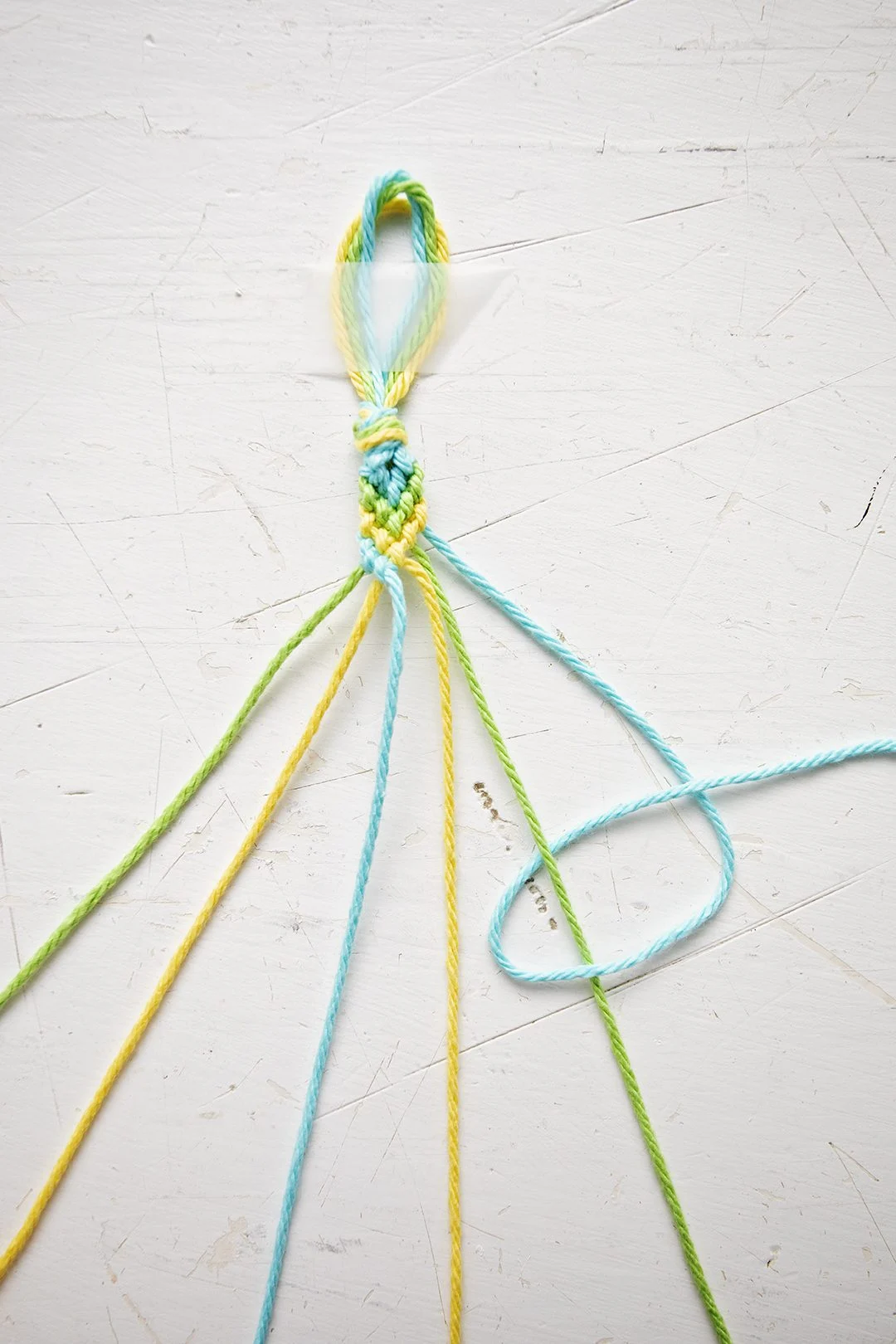 Um padrão de pulseira em Chevron sendo feito a partir de fios azuis, verdes e amarelos.
