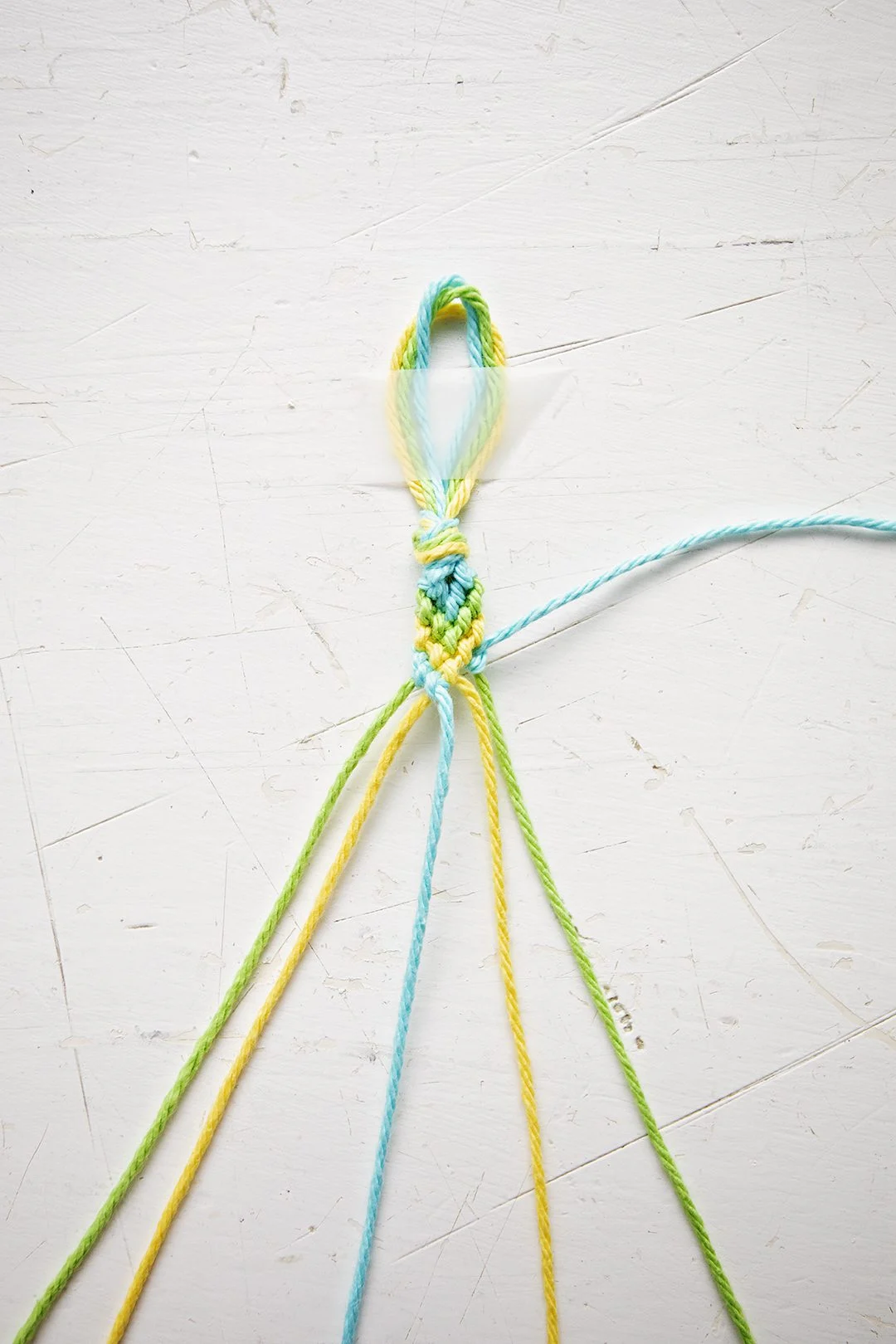 Um padrão de pulseira em Chevron sendo feito a partir de fios azuis, verdes e amarelos.