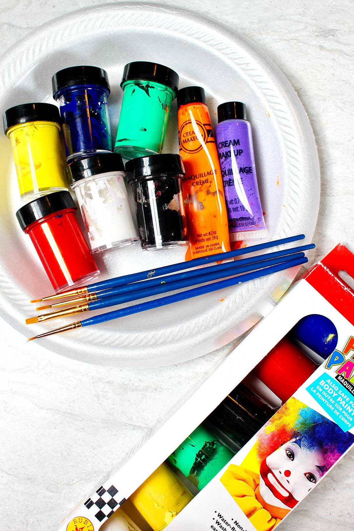 Prato branco com recipientes de tintas coloridas e pincéis de pintura ao redor.