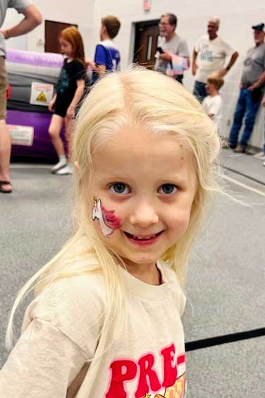 Menina jovem com cabelo loiro com pintura facial de unicórnio.