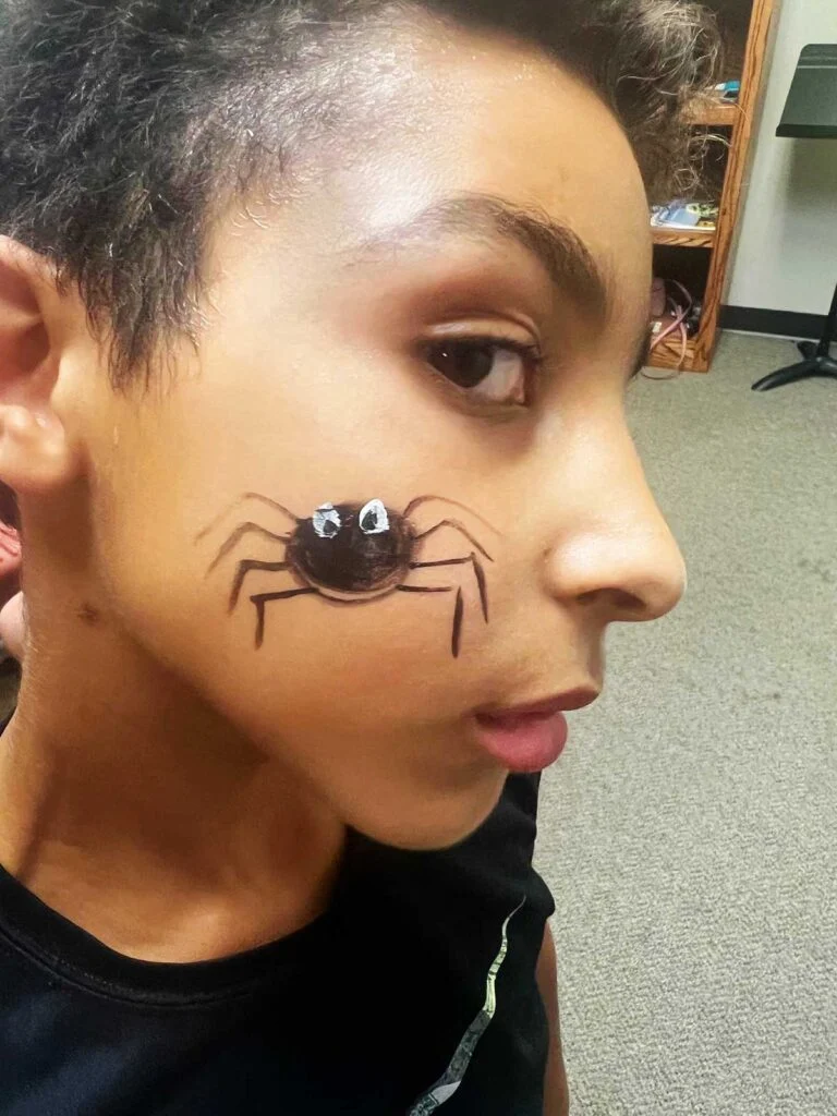 Menino jovem com uma camisa preta com pintura facial de aranha preta.