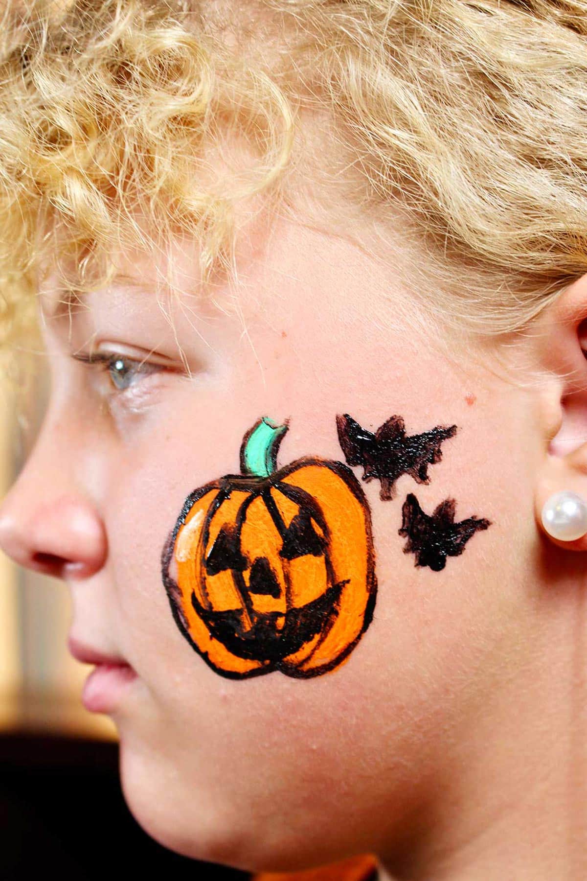 Perfil de uma garota com jack-o-lantern finalizado e dois morcegos pretos na bochecha.