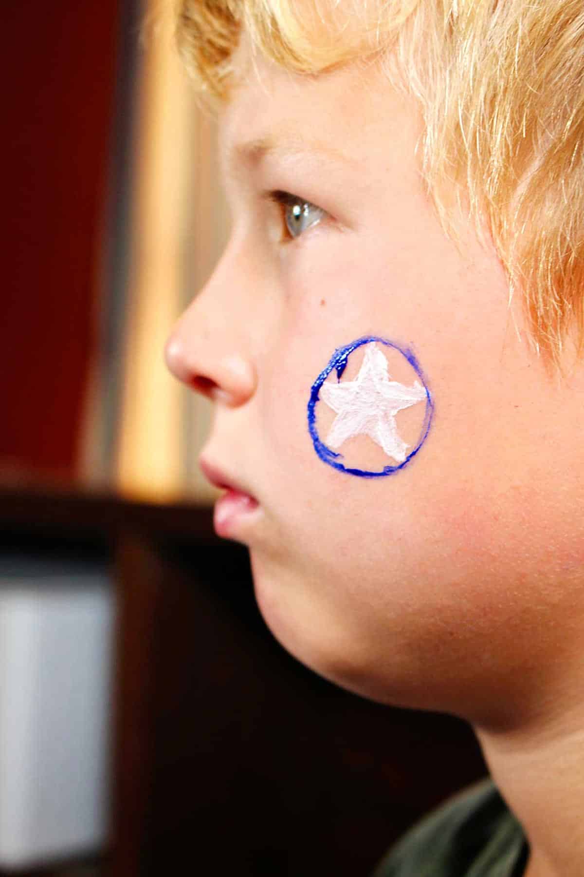 Perfil de menino com estrela branca e círculo azul ao redor pintado na bochecha.