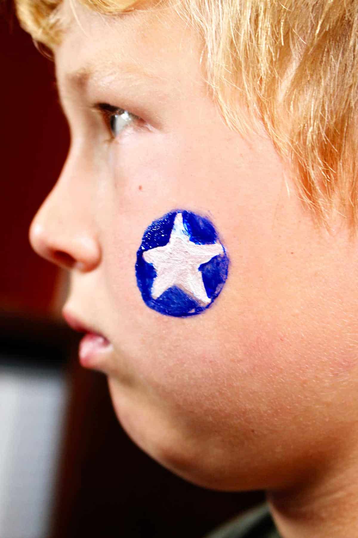 Perfil de menino com círculo azul e estrela branca pintada na bochecha.