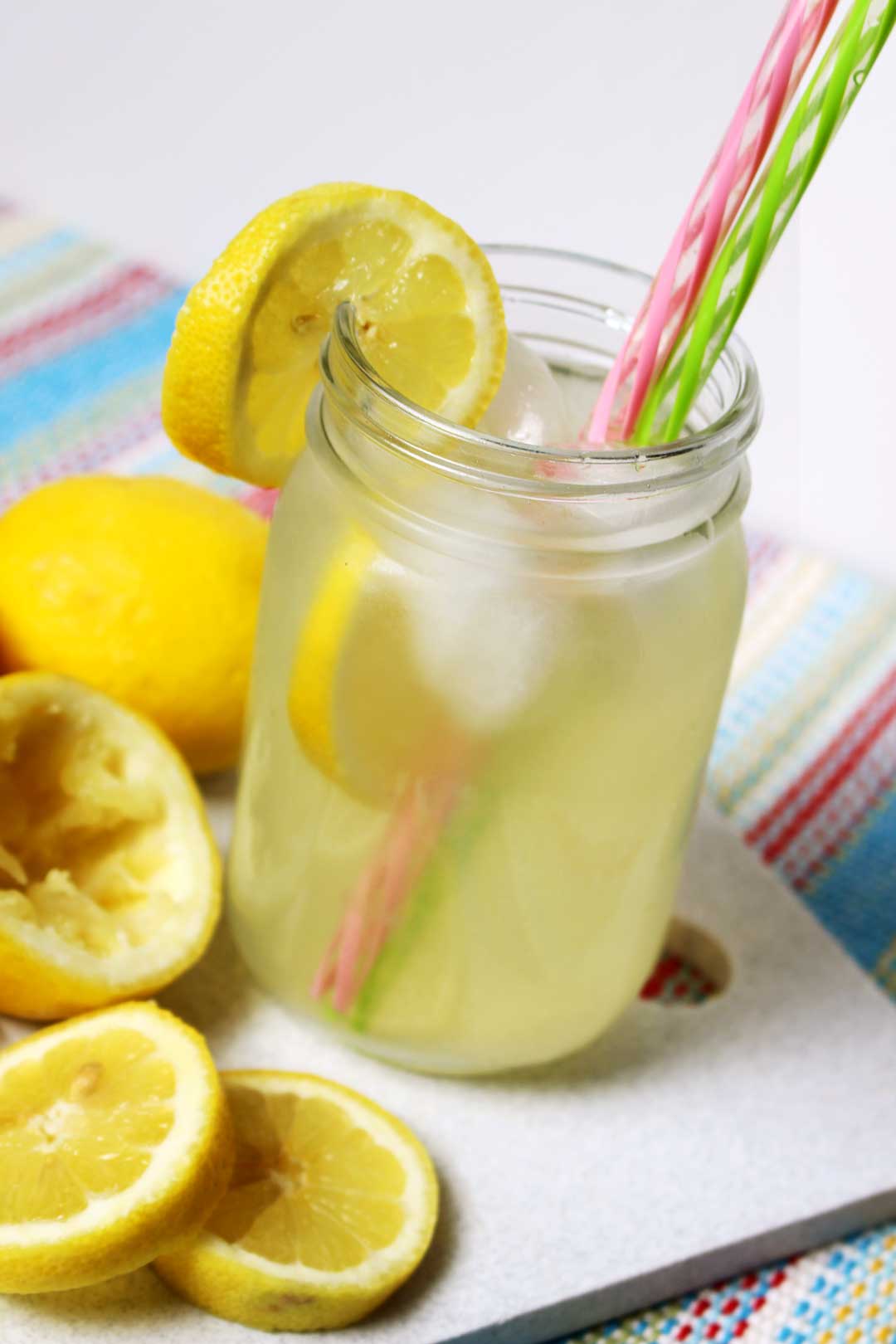 Um copo de limonada em um pote de conserva com canudos rosa e verde perto de algumas fatias de limão.