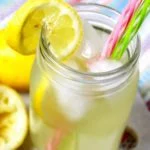Um copo de limonada em um pote de conserva com canudos rosa e verde perto de algumas fatias de limão.
