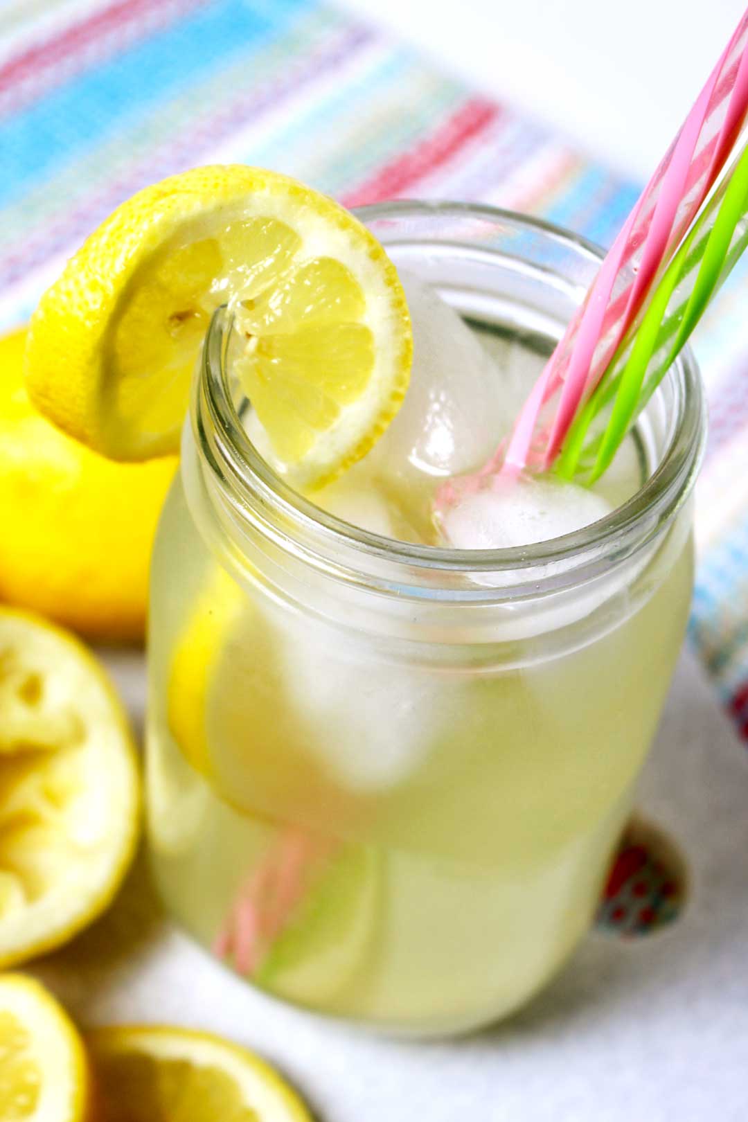Um copo de limonada em um pote de conserva com canudos rosa e verde perto de algumas fatias de limão.