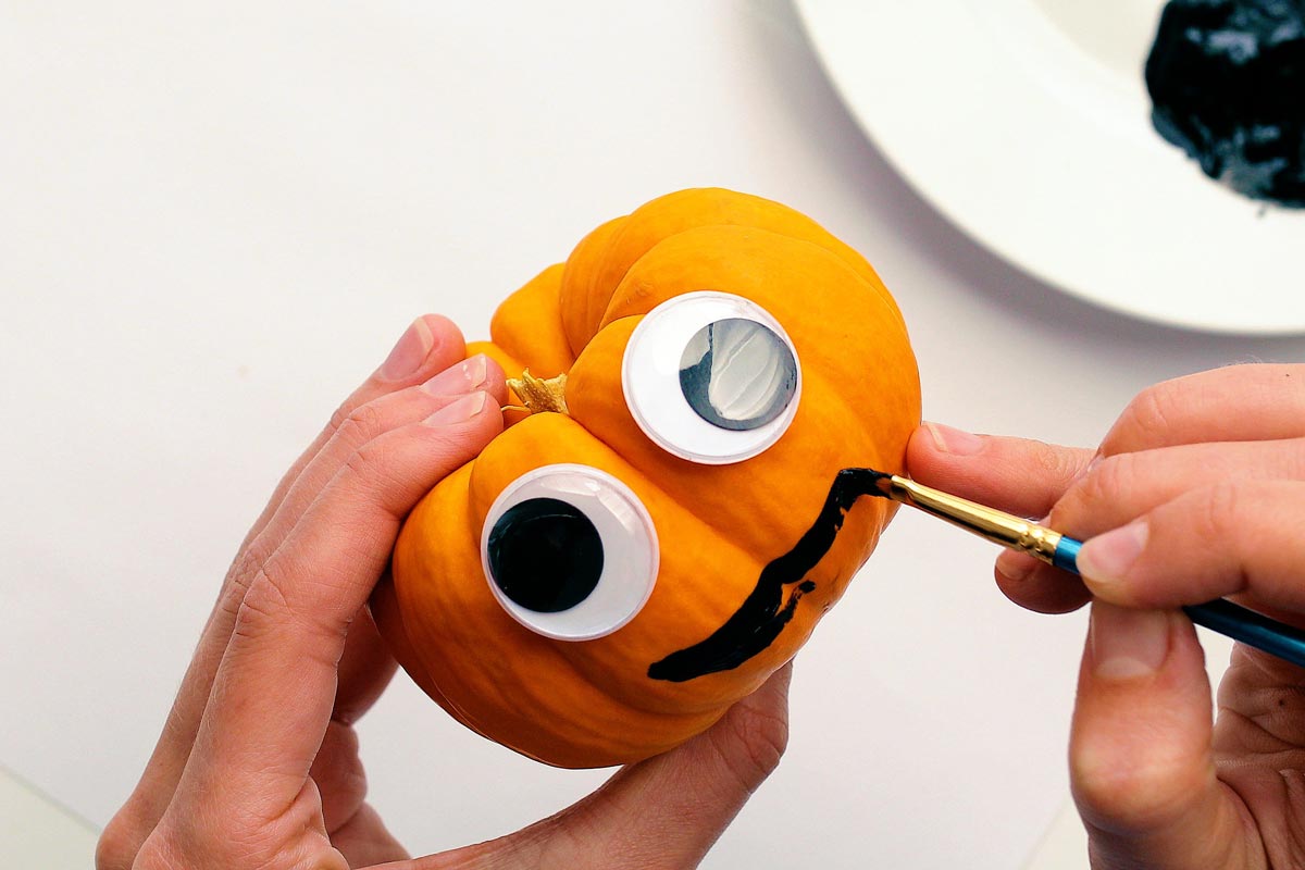 Pintando um sorriso em uma mini abóbora com olhos móveis.