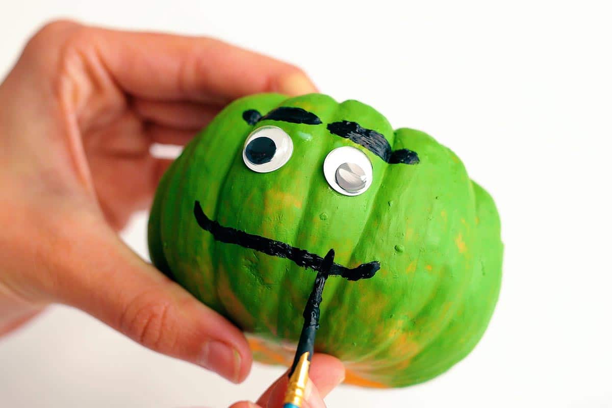 Pincel adicionando sorriso a um rosto de frankenstein em uma artesanato de abóbora.