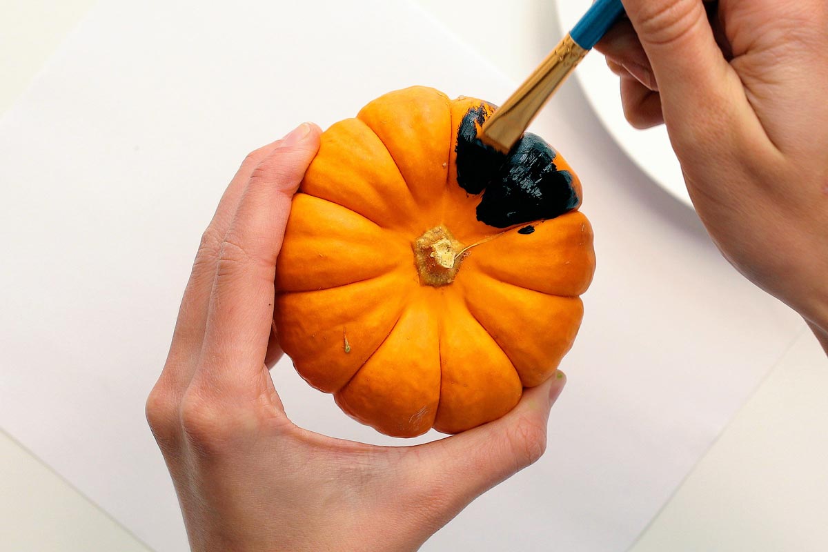 Um pincel pintando uma mini abóbora de preto.