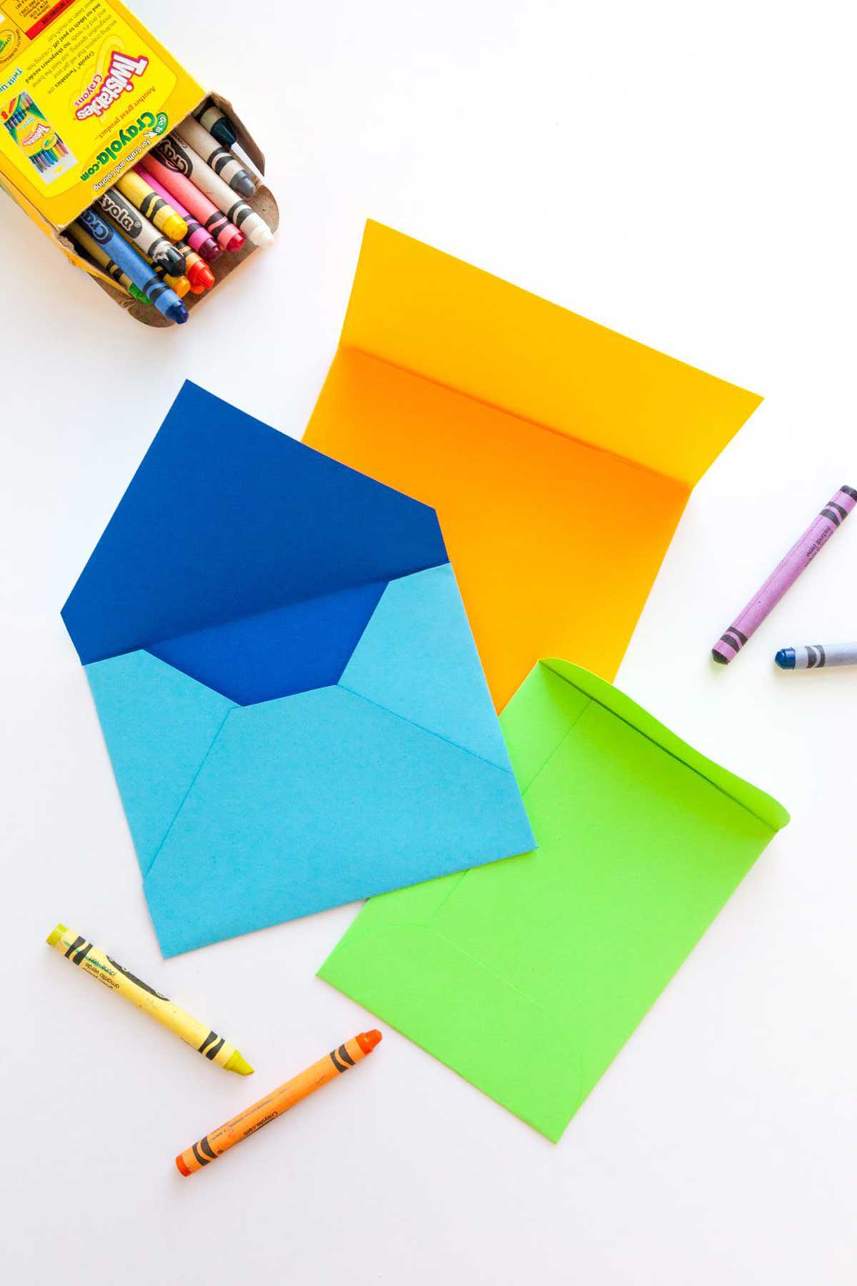Um envelope artesanal azul, verde e laranja cercado por giz de cera.