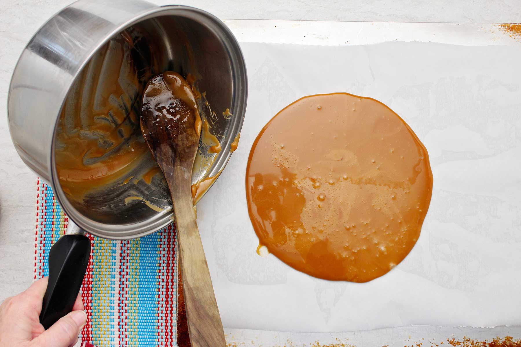 Uma pessoa despejando a mistura de tâfee no papel manteiga.