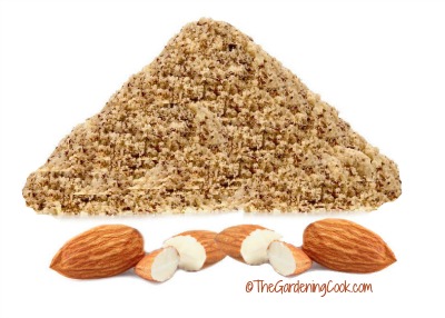 Farinha de amêndoas em uma pilha acima de uma fileira de amêndoas cruas.
