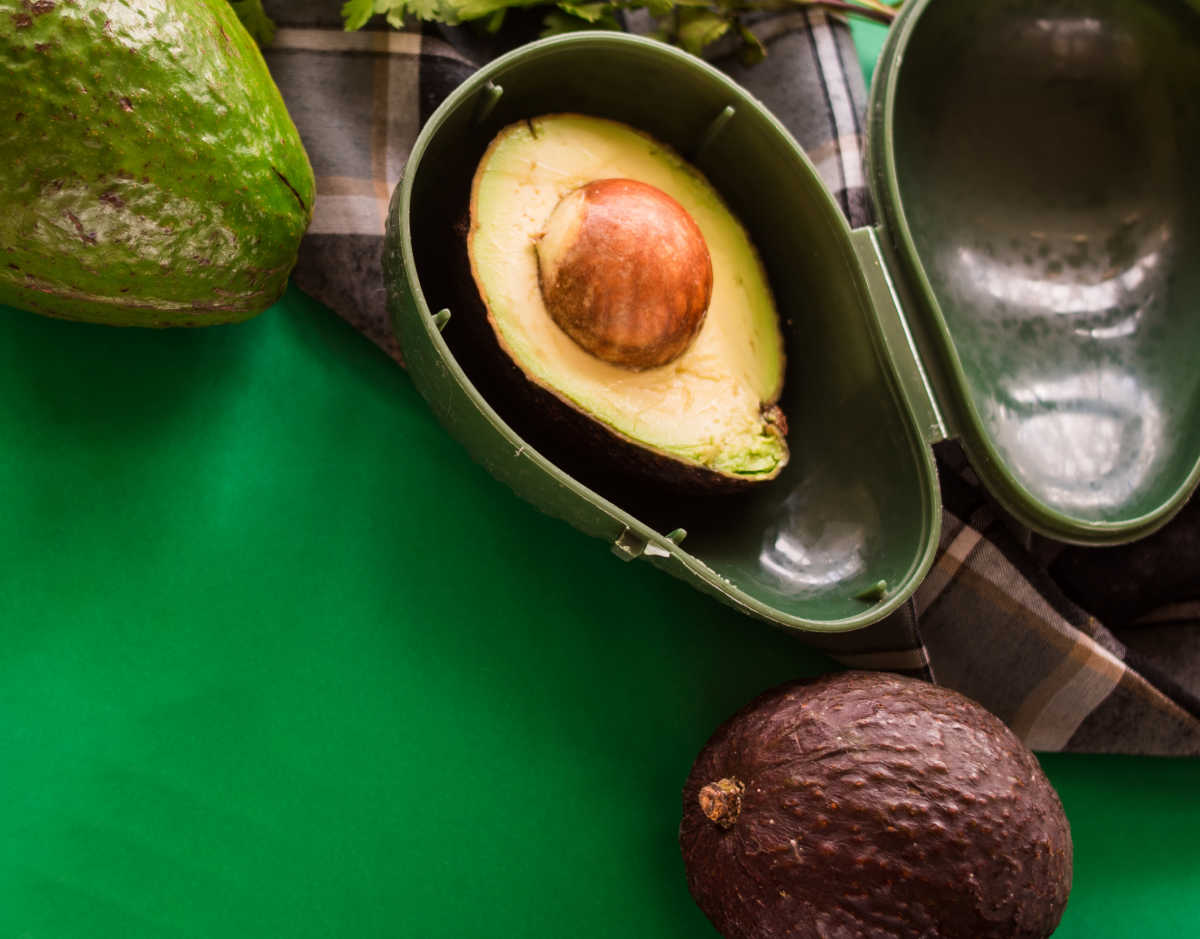 Metade de abacate em um recipiente verde de armazenamento de abacate com um abacate inteiro.