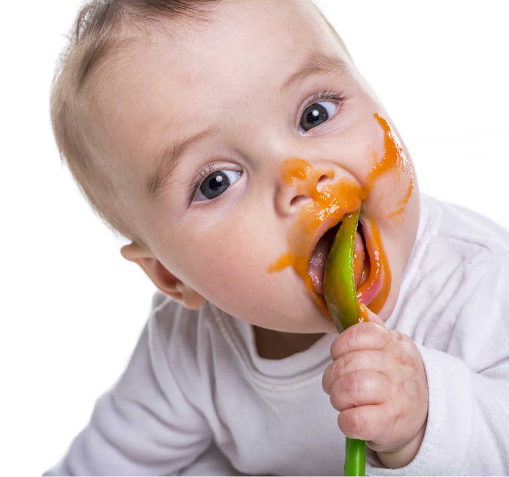 Bebê com colher e comida no rosto.