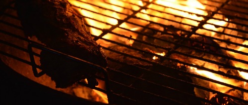 Brasas de churrasco sob uma grelha em chamas.