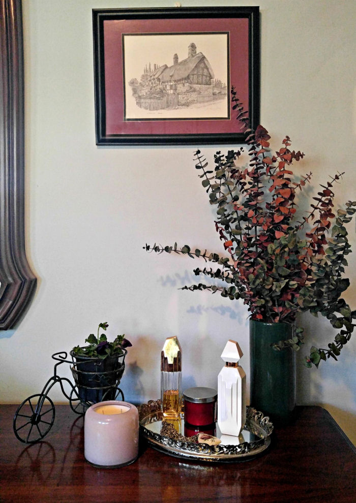 Uma exibição em uma cômoda de quarto com uma impressão de parede, flores secas, planta, bandeja com perfumes e uma vela em um suporte de vidro. Decoração instantânea para o quarto!